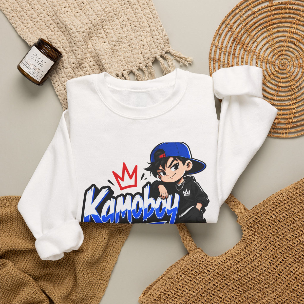 White Kamoboy Crown Crew Sweatshirt flat lay with knit throws and a woven tote, showing the colorful front graphic