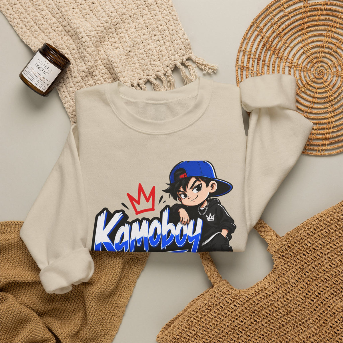 Sand Kamoboy Crown Crew Sweatshirt flat lay with knit throws and a woven tote, showing the colorful front graphic